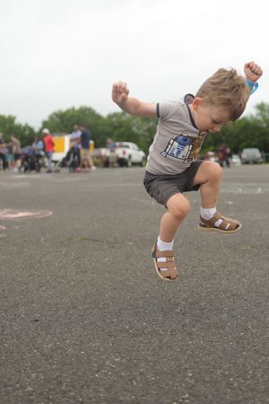 Small child in a Star Wars t-shirt and sandals jumping excitedly in a parking lot with people and cars in background.