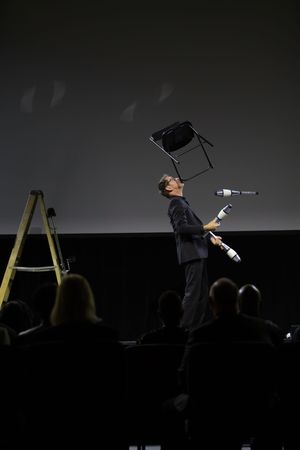 A musician performs with dramatic lighting on stage while holding a conductor's baton in a theatrical setting.