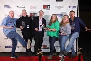 Group of people posing together on red carpet with drinks at what appears to be a media or entertainment event.