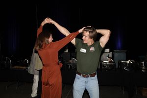 Two people are dancing together at a night event with dark lighting and stage equipment in the background.