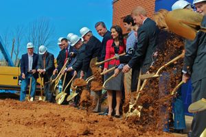 Groundbreaking ceremony where people stand in line with shovels to dig into red clay soil during a construction event.