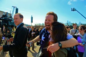 People share a joyful moment while surrounded by cameras and film equipment on a sunny day outdoors.