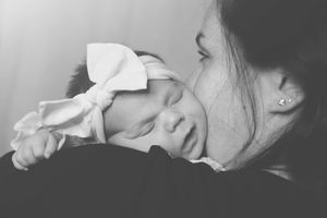 Black and white close-up of baby wearing white bow peacefully resting against someone's shoulder.