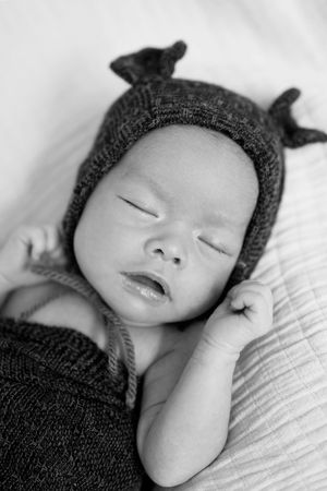 Sweet sleeping newborn wearing a charming gray knit hat with tiny ears while resting on soft white bedding.