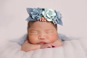 Baby sleeping peacefully with delicate blue floral headband against soft pink background.