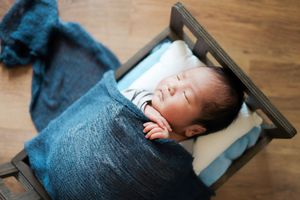 A tiny newborn rests peacefully under a gray blanket while laying in a wooden prop bed.
