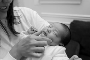 A close-up black and white photo shows a young infant being held while gently touching their face.