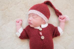 Sleeping newborn wearing cozy red knitted outfit with white trim and matching hat lying on soft white blanket.