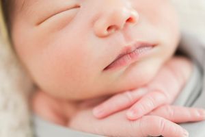 Close up view of a soft sleeping baby's face with delicate features against a white backdrop.