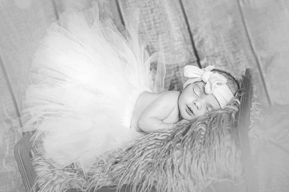 A black and white artistic portrait of someone reclining on a furry surface wearing a tulle skirt with dreamy lighting effects.