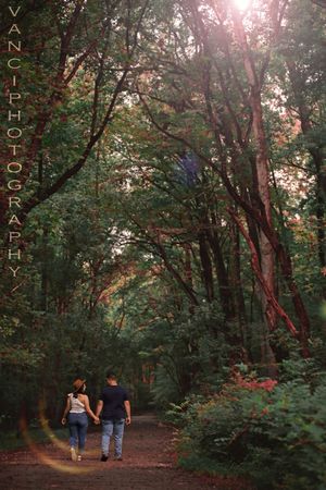 Two people walking together on a scenic forest trail during golden hour as sunlight filters through tall trees.