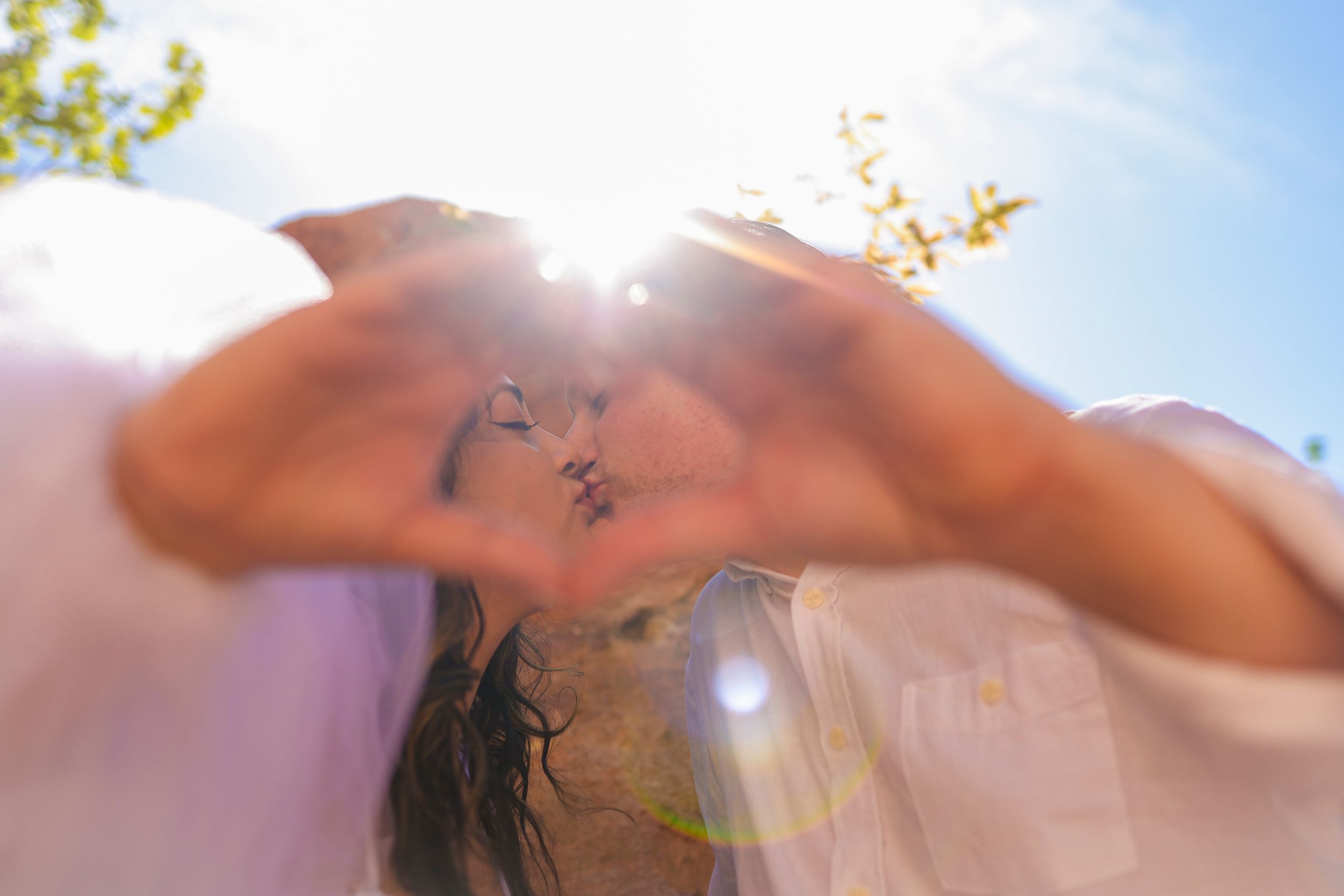 A silhouetted figure stretches their arms up against a bright sunny sky with lens flare and blurred foreground.