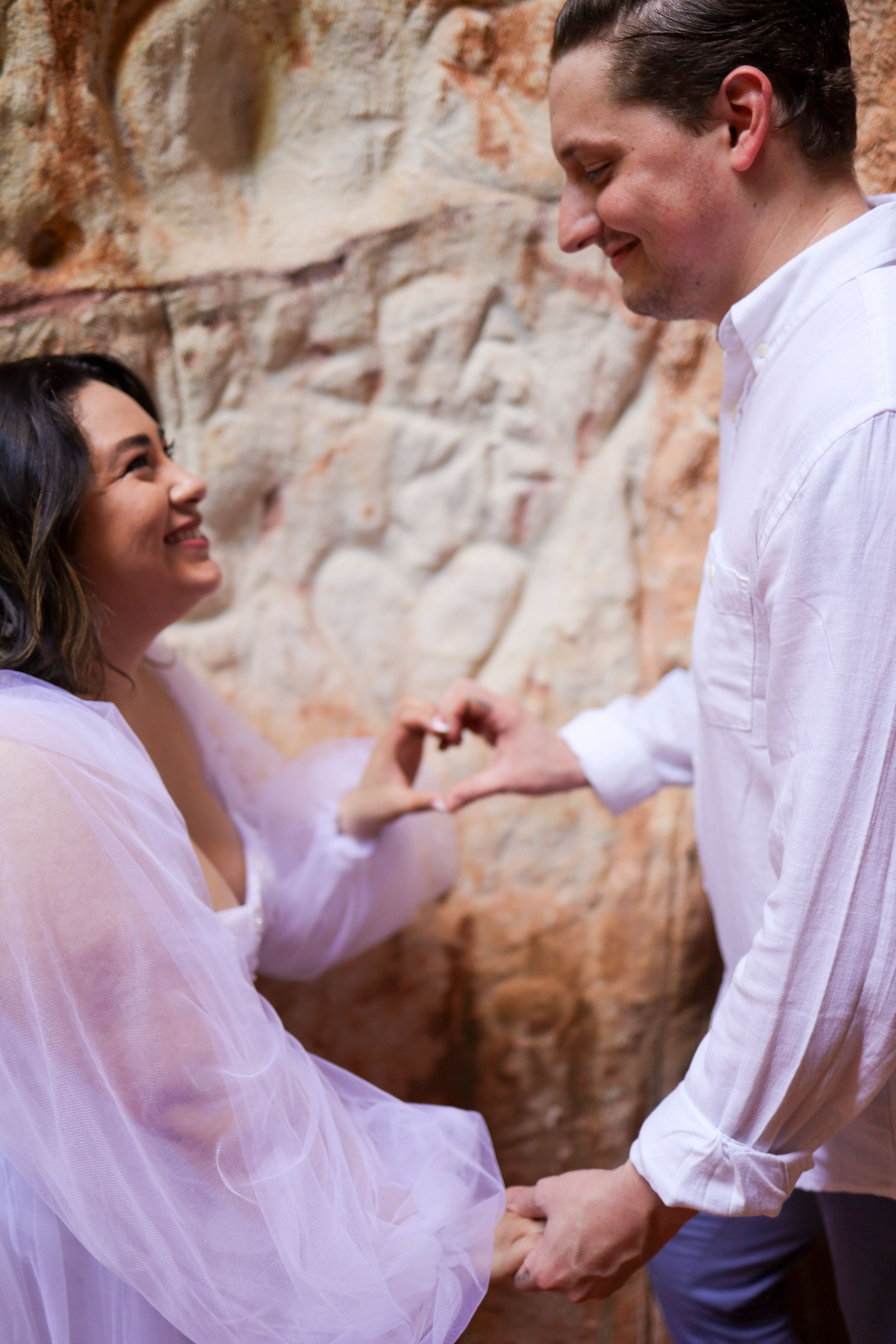 A couple wearing white clothing share an intimate moment against a textured stone wall background.