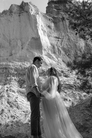 A romantic black and white wedding photo of a couple standing before dramatic white cliffs in a scenic outdoor setting.