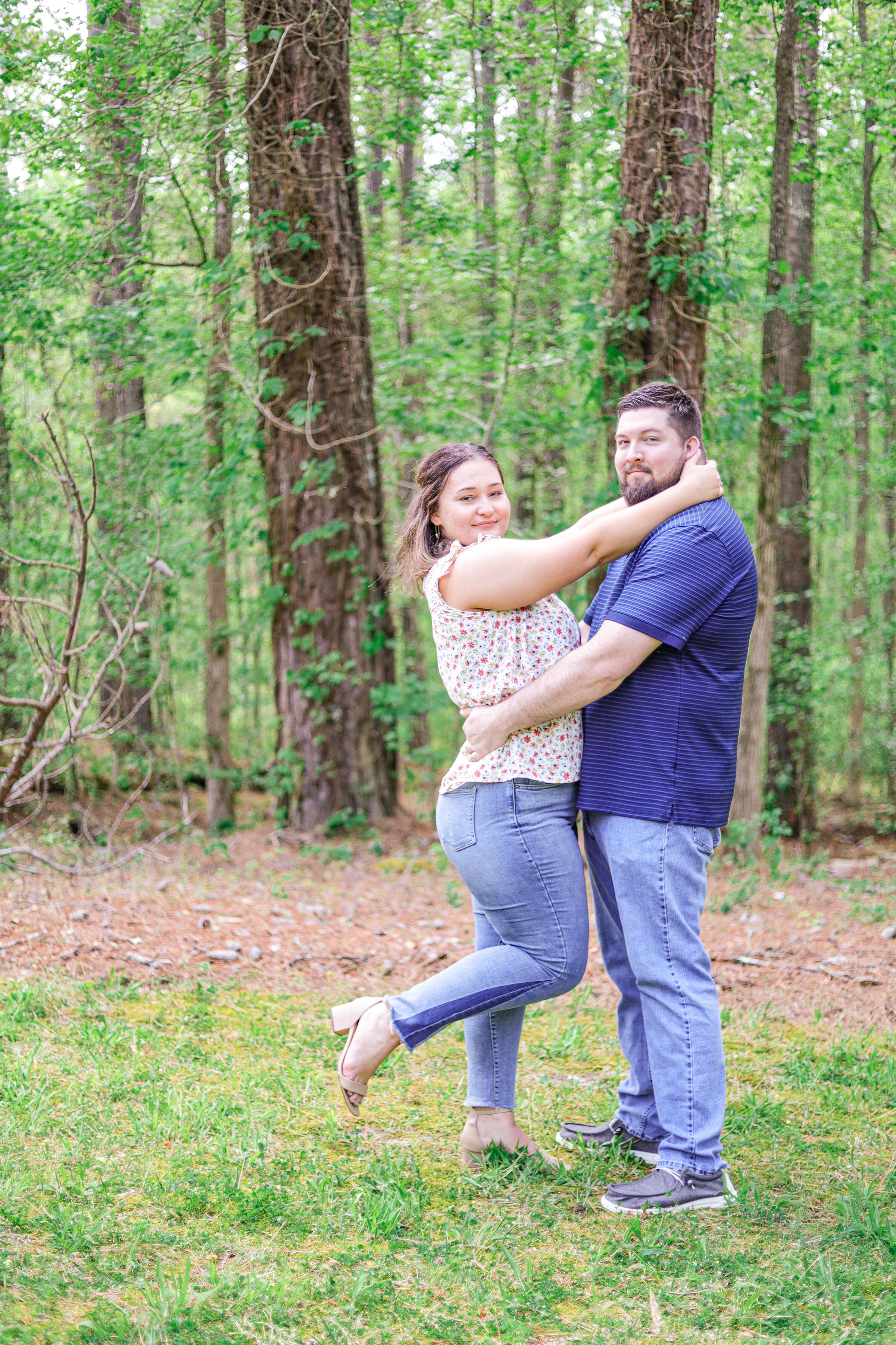 Two people embrace and dance playfully together in a lush green forest setting.
