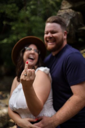 A couple shares a joyful intimate moment during their engagement as they show off a new ring outdoors in the sunlight.