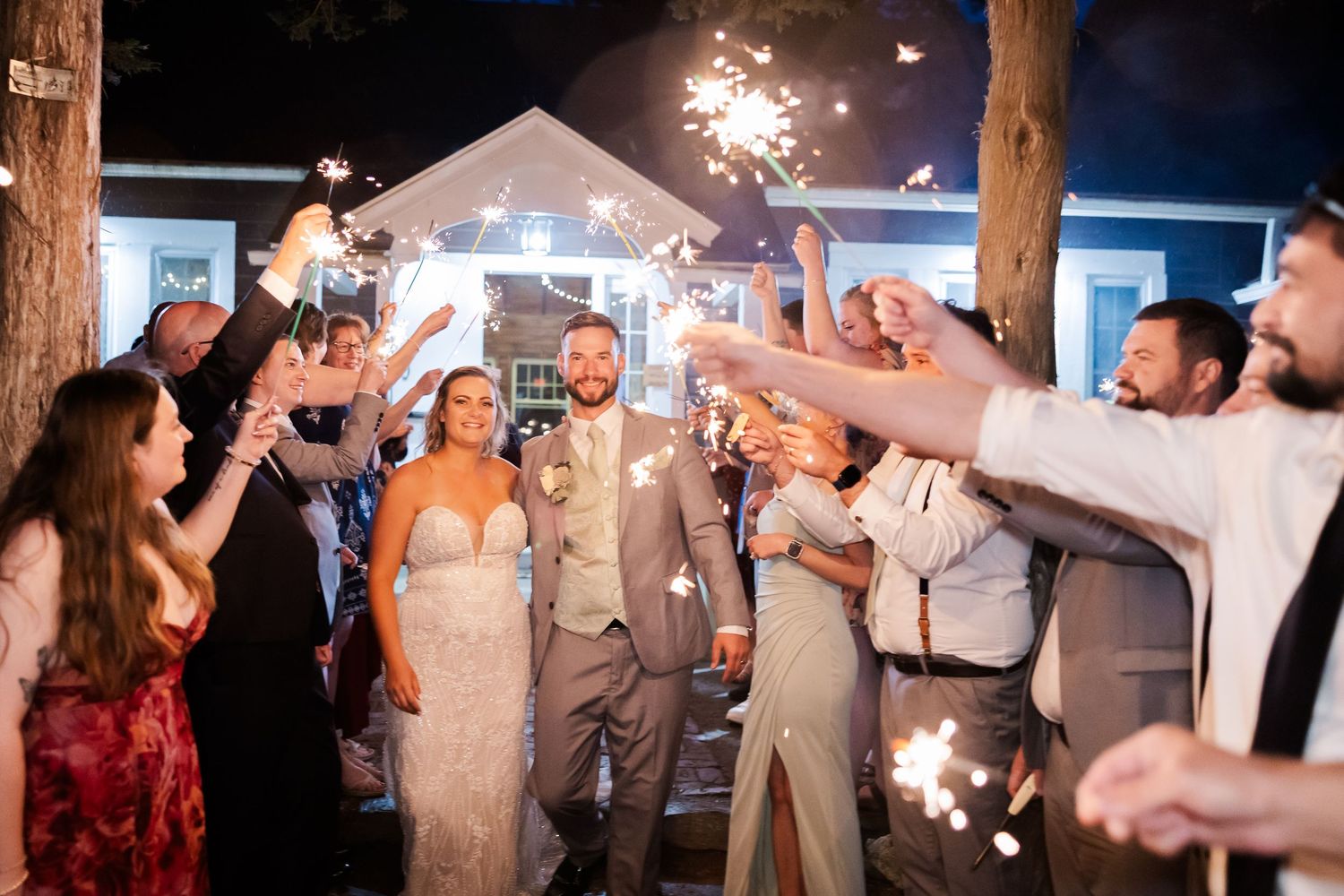 Wedding guests hold sparklers creating a magical nighttime tunnel exit for the newlyweds at a blue venue.