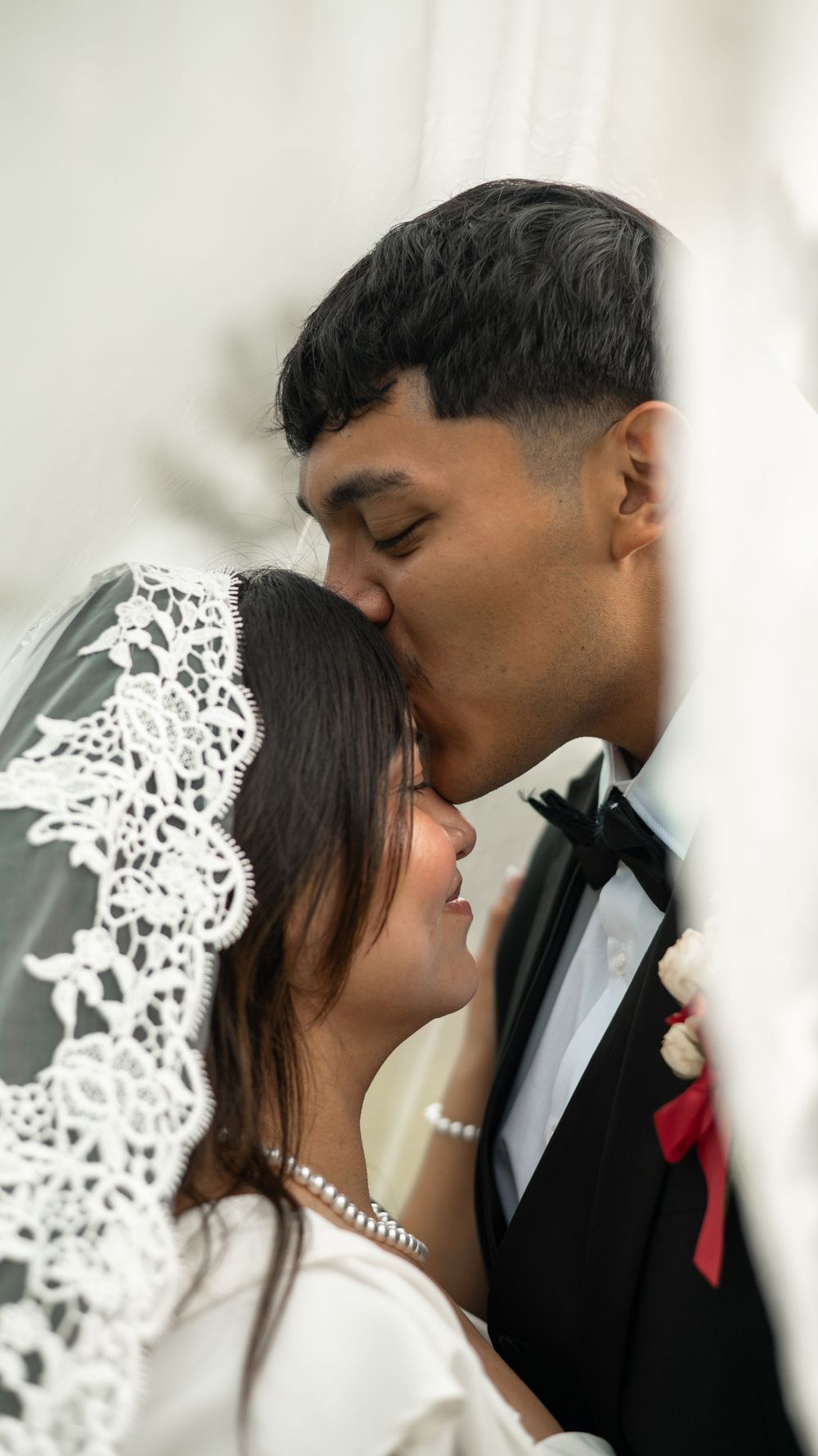 Bride and groom share intimate moment under delicate lace veil during wedding portrait session.