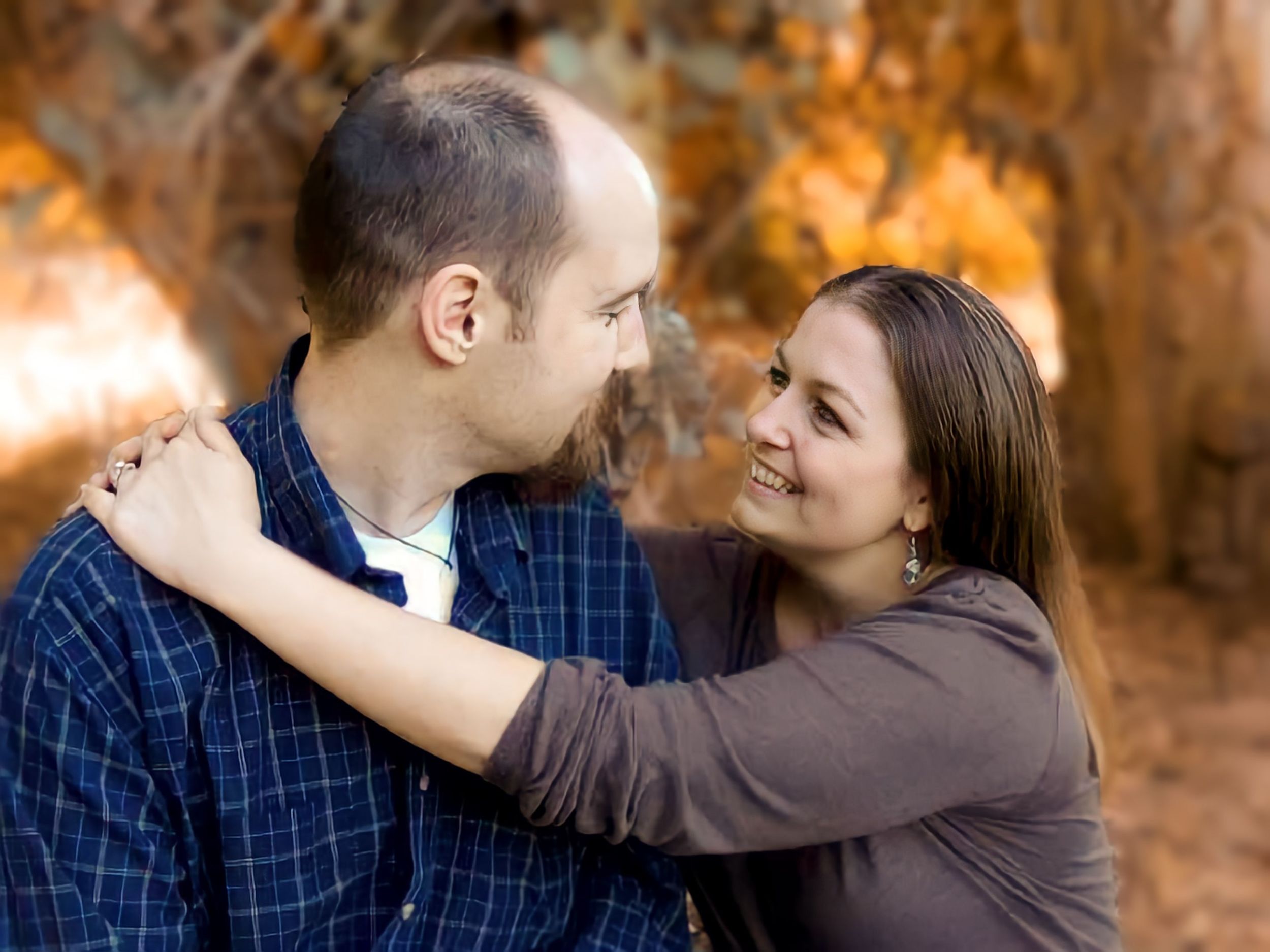 A couple shares a romantic embrace while looking at each other against a backdrop of autumn foliage.