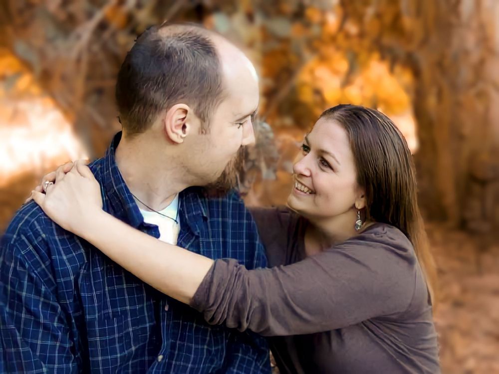 A couple shares a romantic embrace while looking at each other against a backdrop of autumn foliage.