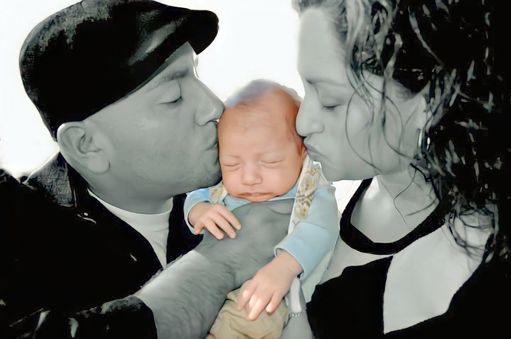 A sleeping baby being gently held and kissed by loving parents in a tender family moment.
