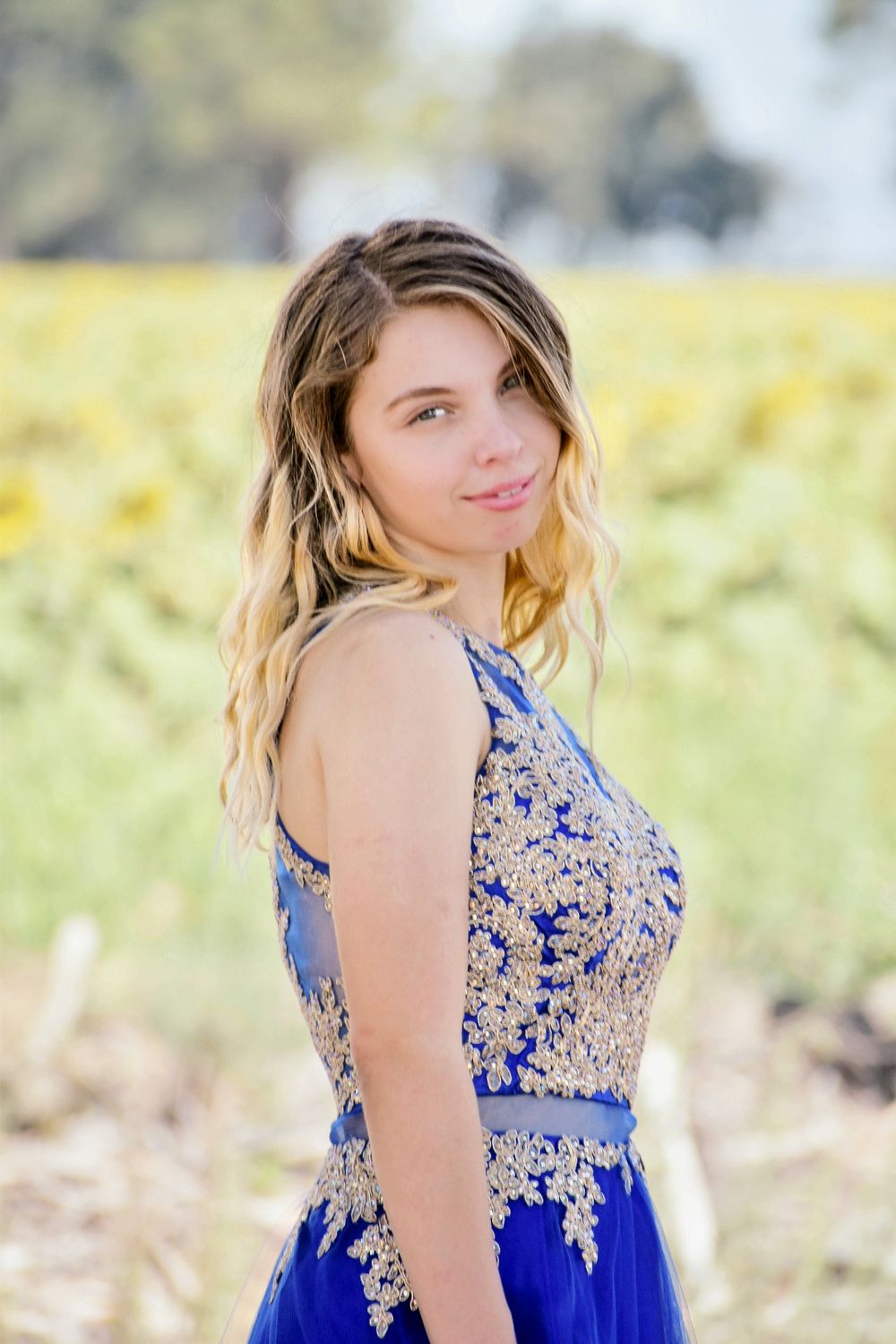 Portrait in a field of yellow flowers featuring a blue formal dress with lace details.