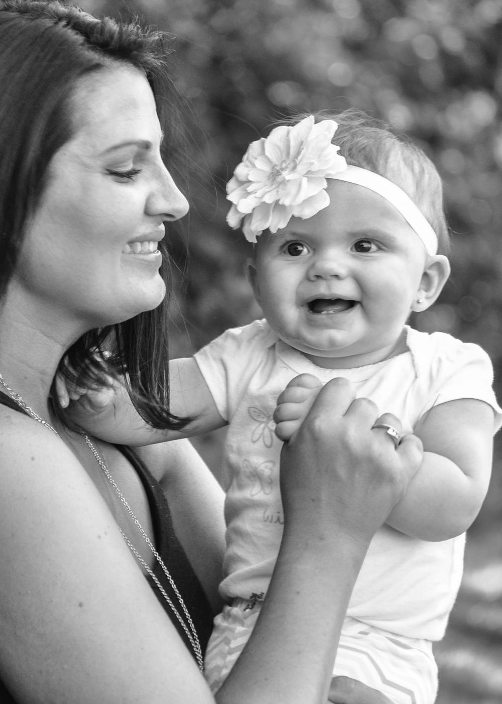 A tender black and white portrait of joyful interaction between an adult and happy baby wearing a white floral headband.