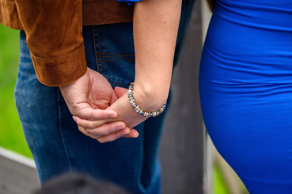 A couple holds hands tenderly while wearing casual attire of blue and brown.