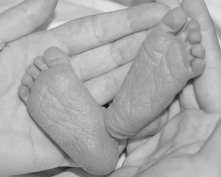 A black and white close-up of tiny newborn baby feet being gently cradled in adult hands.