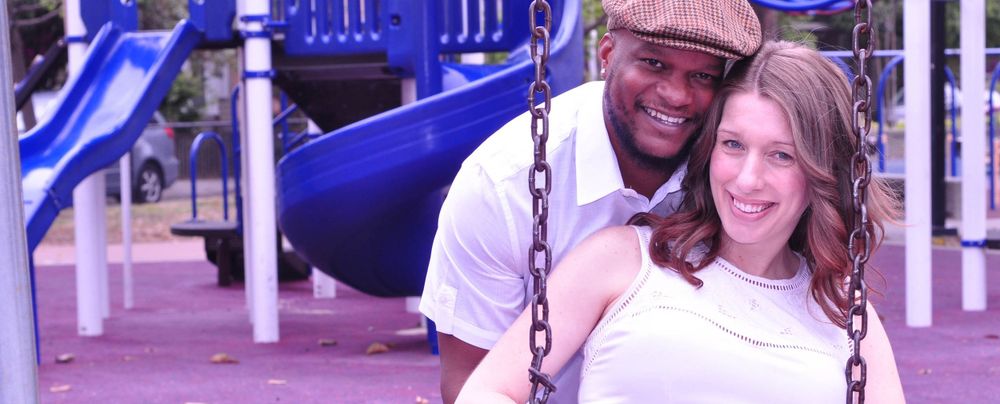 Two people smile while sitting together on playground swings on a sunny day.