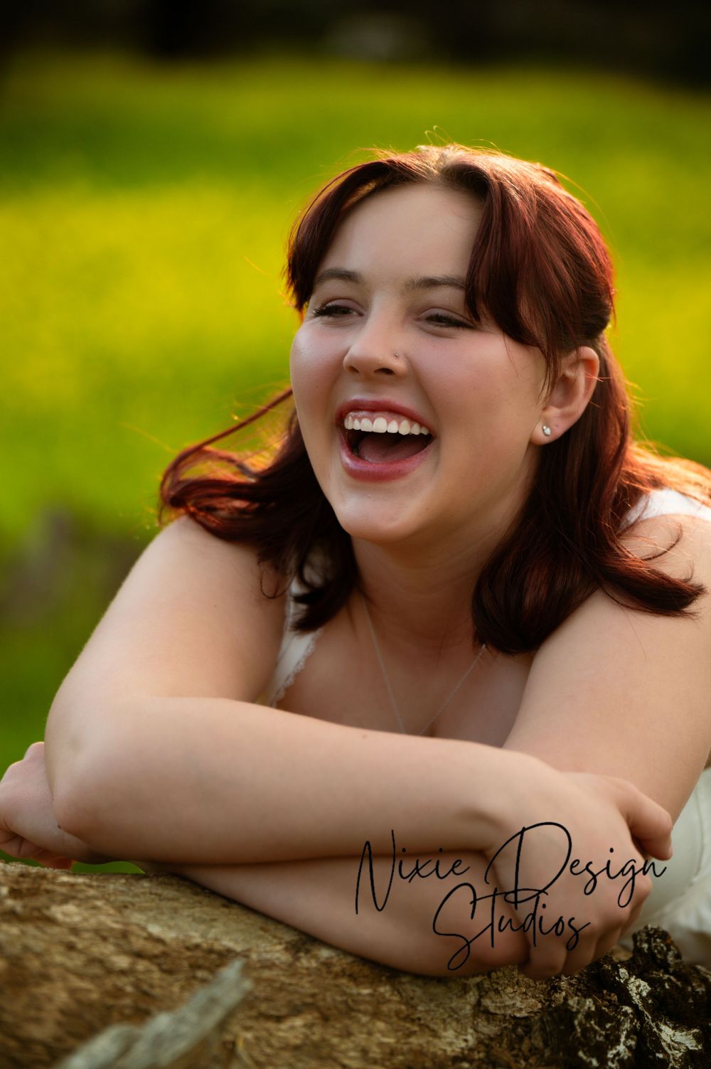 A joyful portrait captured outdoors against a green background with natural lighting and watermark.