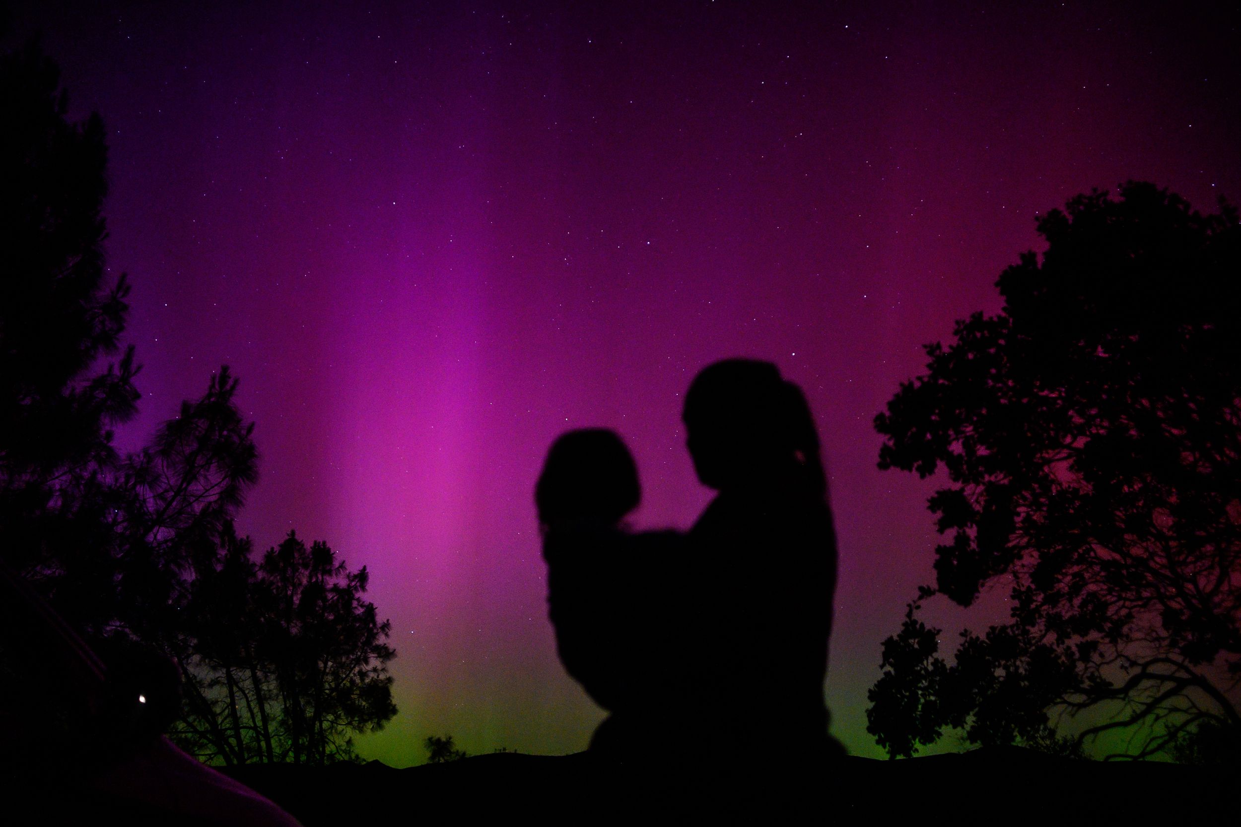 Silhouette of two figures against a dramatic purple sky with green aurora borealis along the horizon.