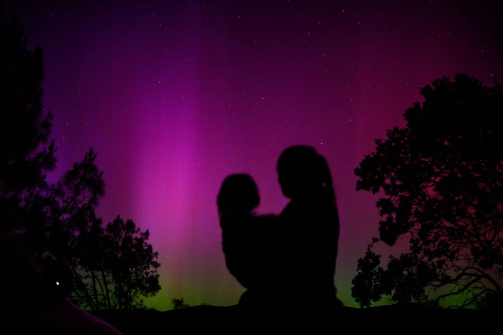 Silhouette of two figures against a dramatic purple sky with green aurora borealis along the horizon.