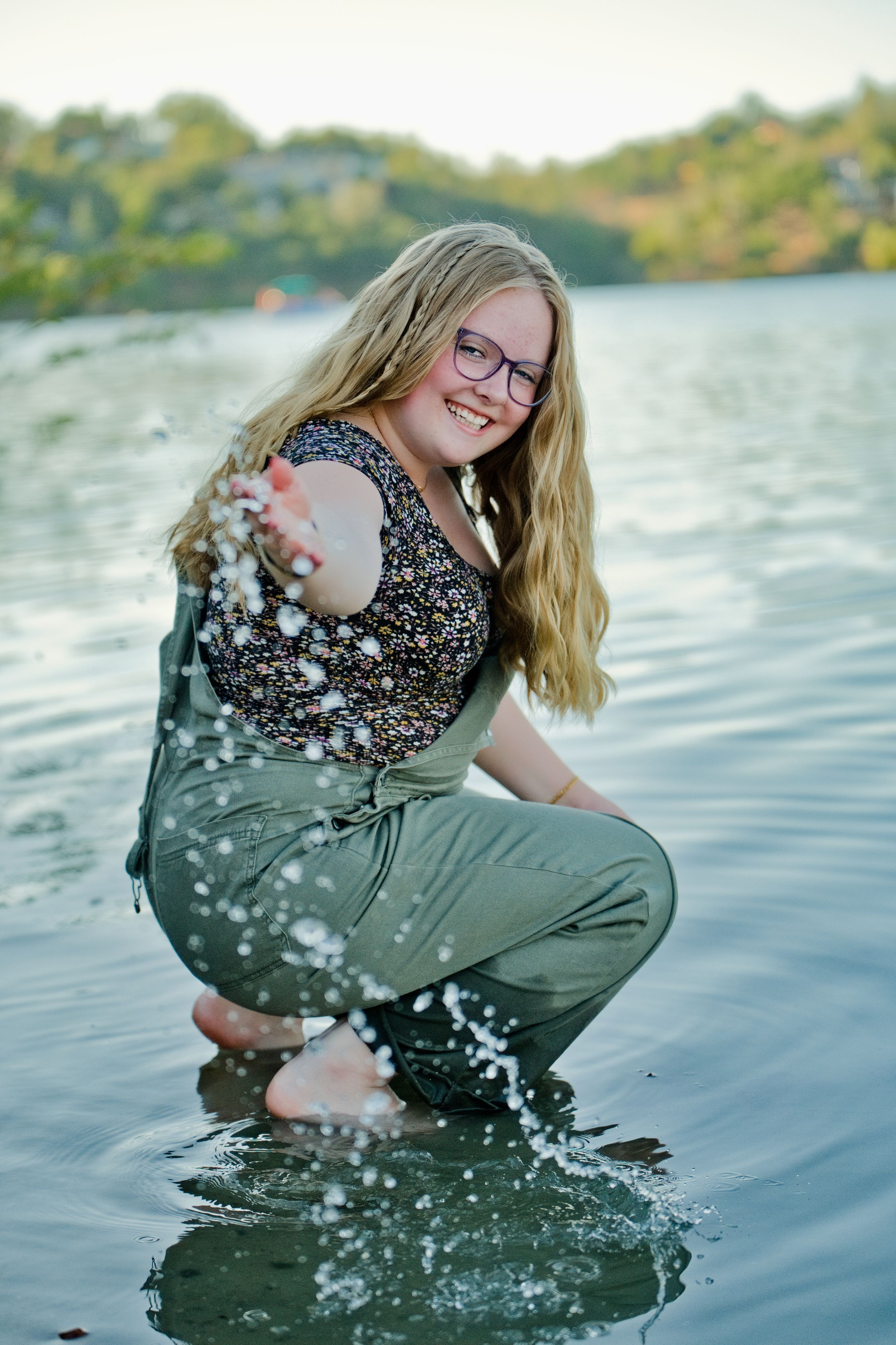 A happy figure wearing eyeglasses splashes playfully in a lake at sunset, creating water droplets in the air.
