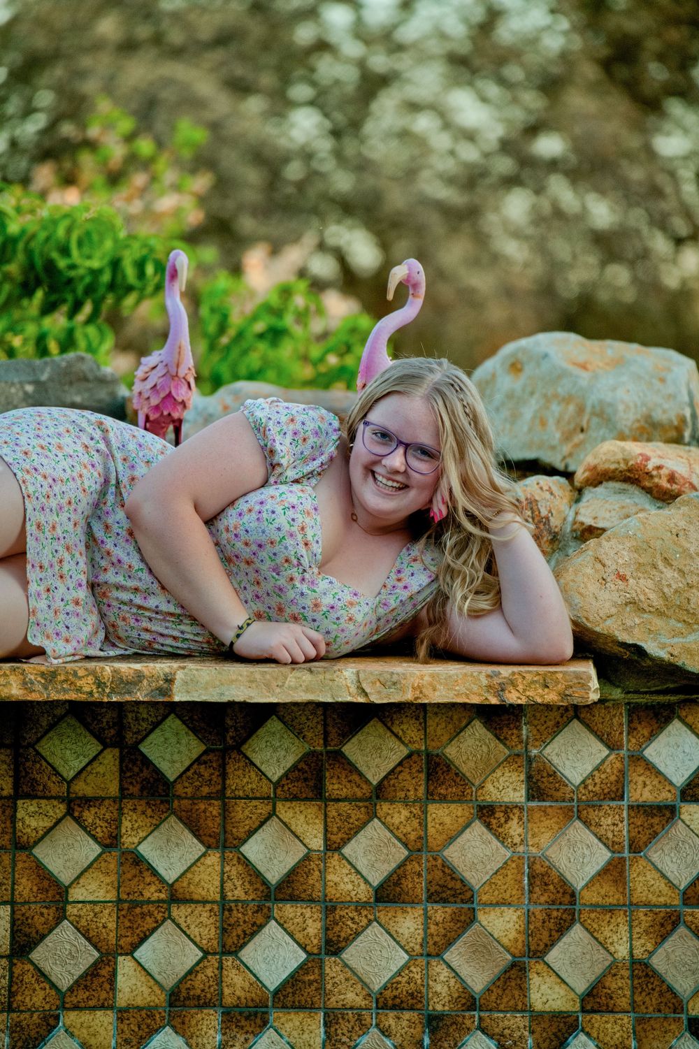 A relaxed outdoor portrait with decorative tile and pink flamingo decor in the background.