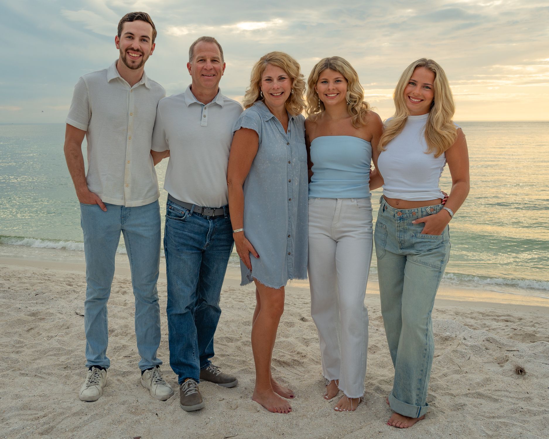 Family group of five poses casually together on beach at sunset wearing coordinated outfits.