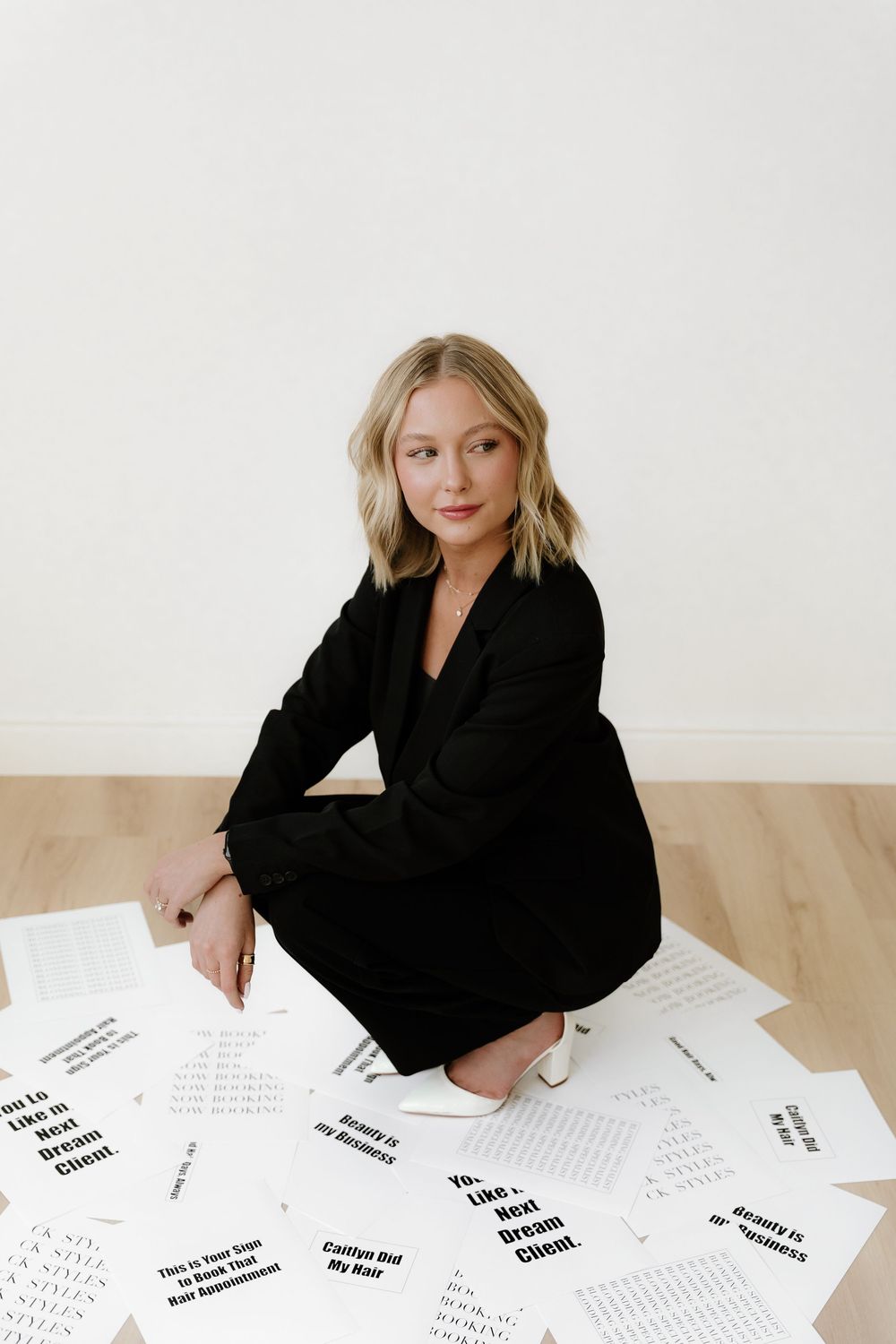 Fashion editorial scene with black suit and papers scattered on light wooden floor.