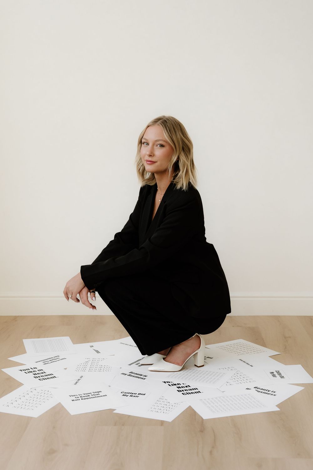 A professional photo shoot featuring a black dress and scattered papers on a wooden floor.