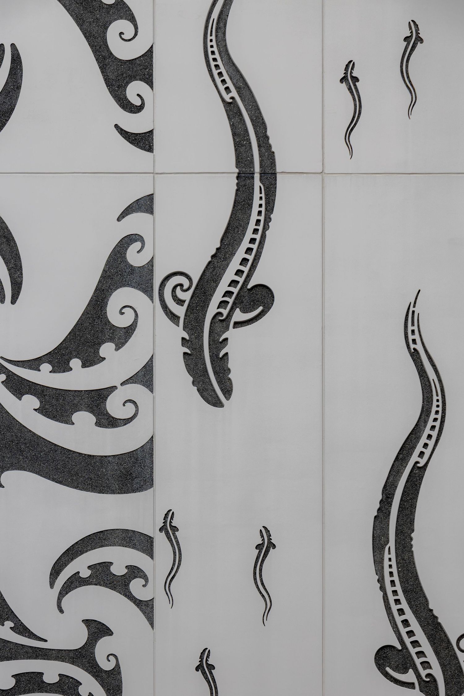 Architectural concrete wall panels featuring Māori-inspired black designs resembling eels and koru shapes.