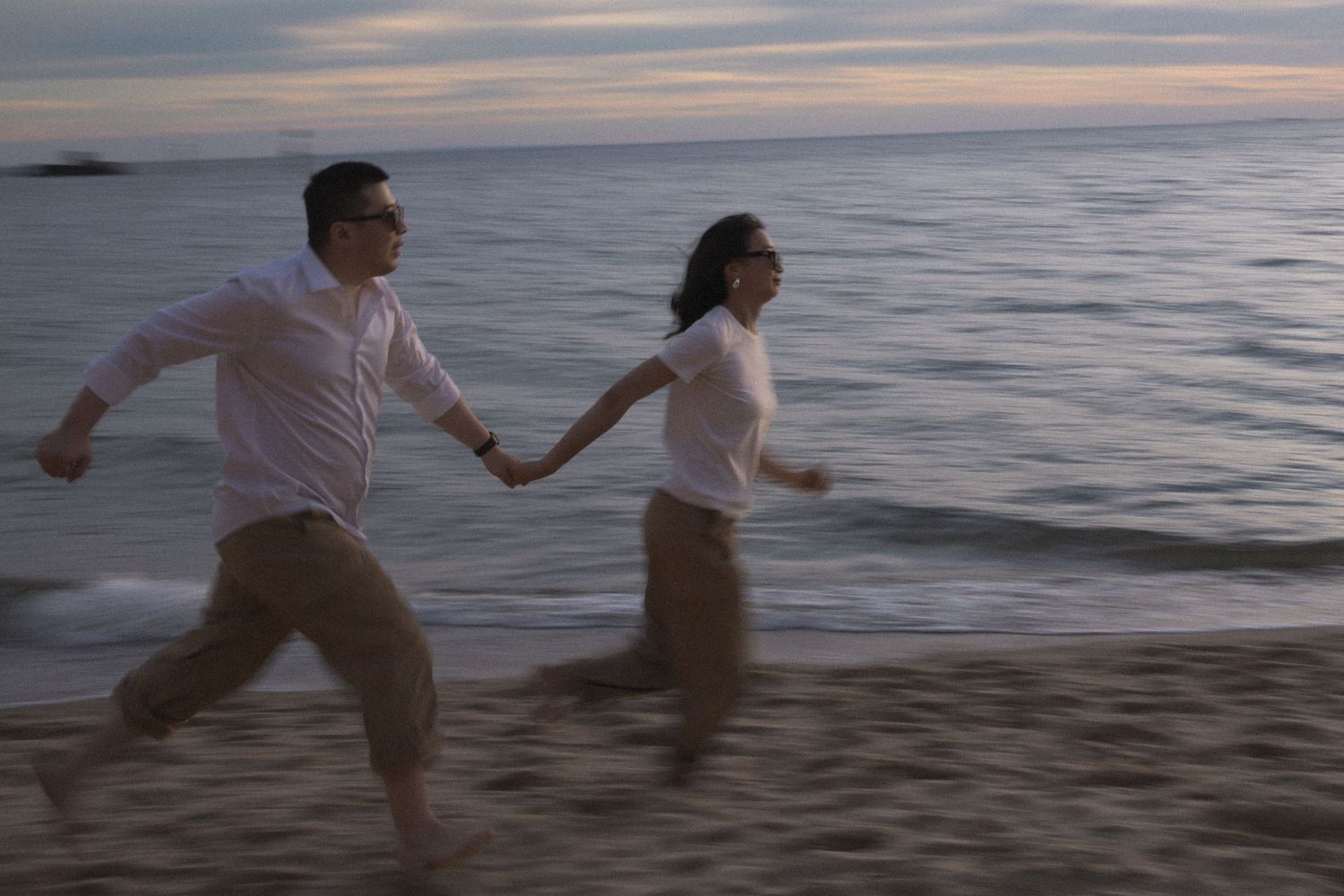 A couple playfully splashes in the ocean at sunset while walking along a sandy beach.