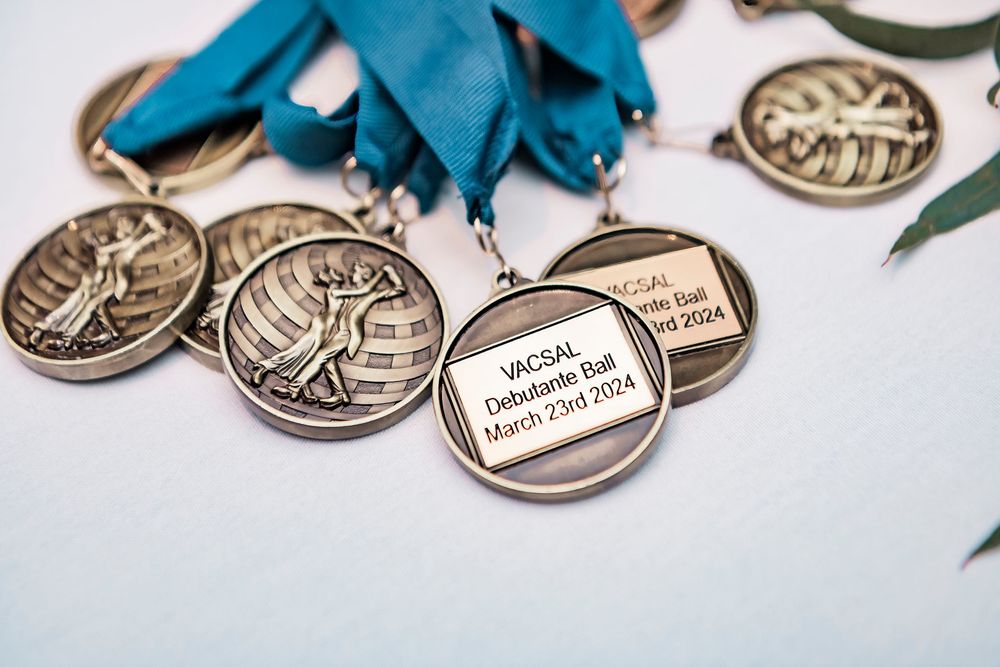 Silver medals with blue ribbons arranged on a white surface showing inscribed texts and similar engravings.