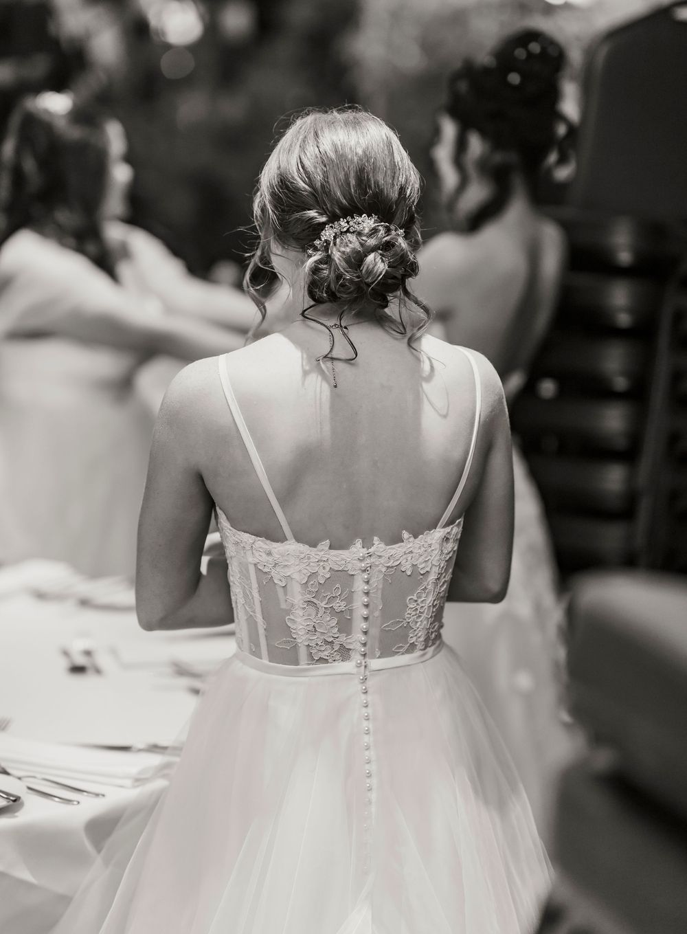 Black and white photo showing the back of a bride wearing a corset-style wedding dress with delicate button details and updo.
