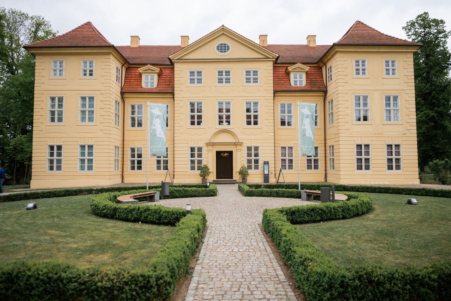 Außenansicht Schloss Mirow mit gelber Fassade und gepflegtem Gartenweg