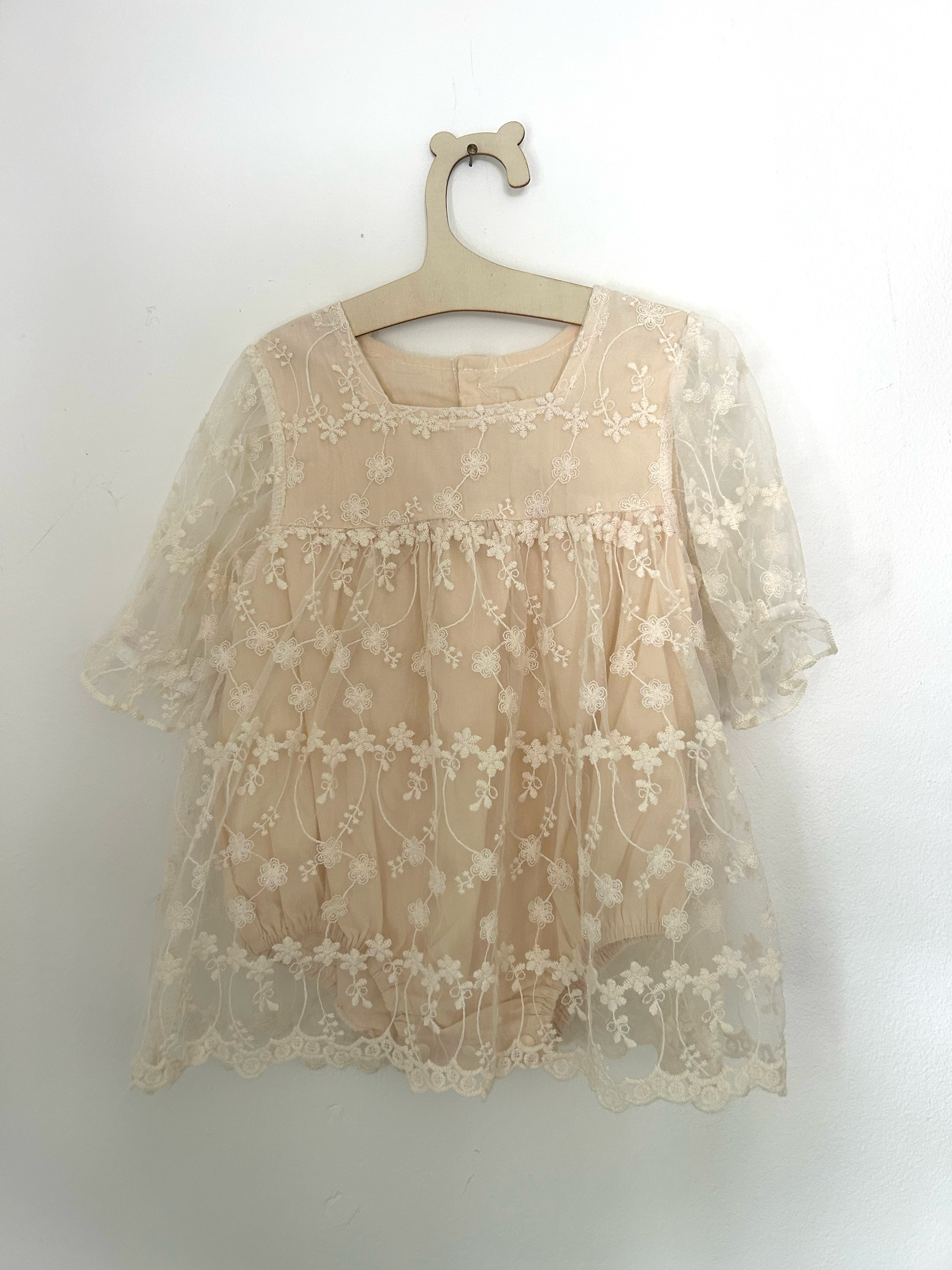 White knit baby romper with 'ONE' text and small bow detail in pink embroidery against hanging clothing background.