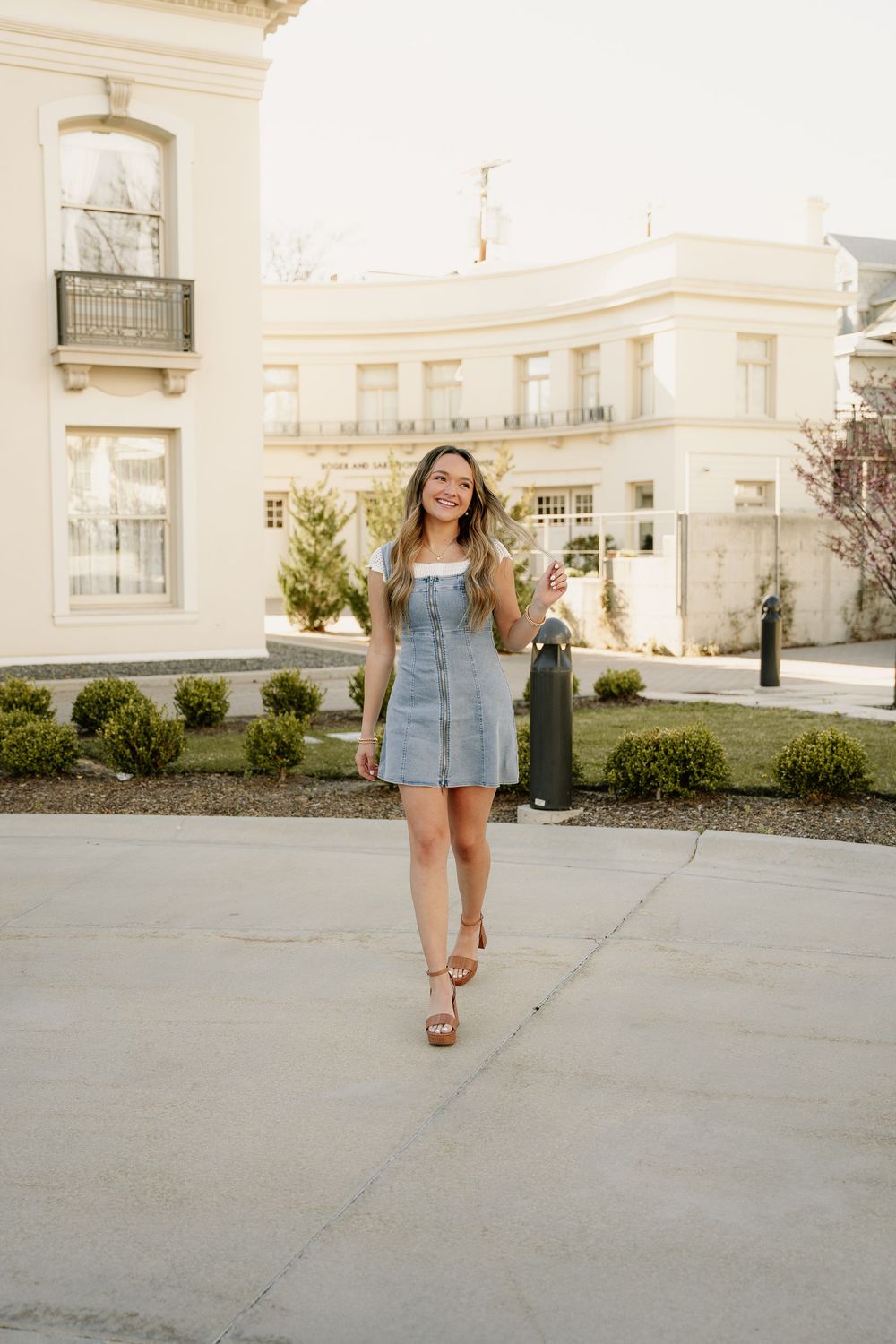 Denim dress outfit photographed in warm golden light against classic building exterior.