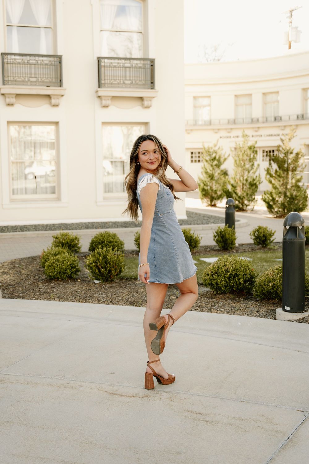 Stylish denim dress and heels outfit captured in front of classic building architecture.