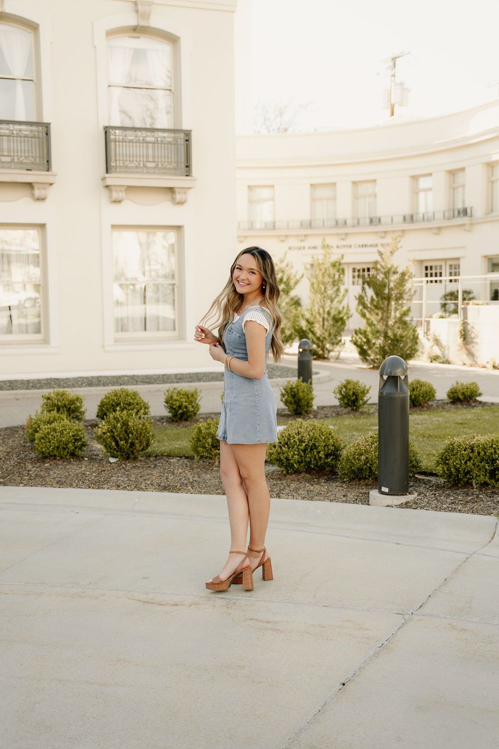 Outdoor fashion portrait by elegant white building wearing denim dress and block heel sandals.