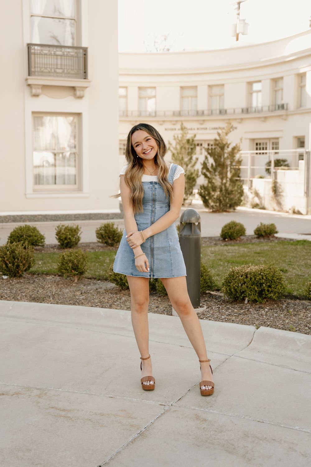Spring fashion portrait in denim dress and platform sandals against curved architectural backdrop.