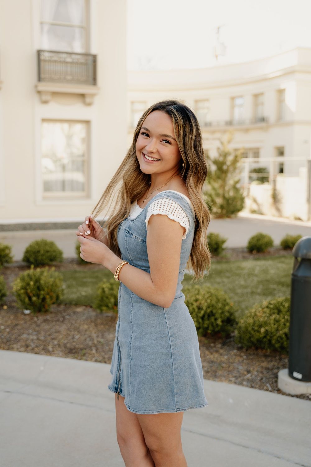 Summer fashion look featuring denim overall dress and white cap sleeve top in garden setting.