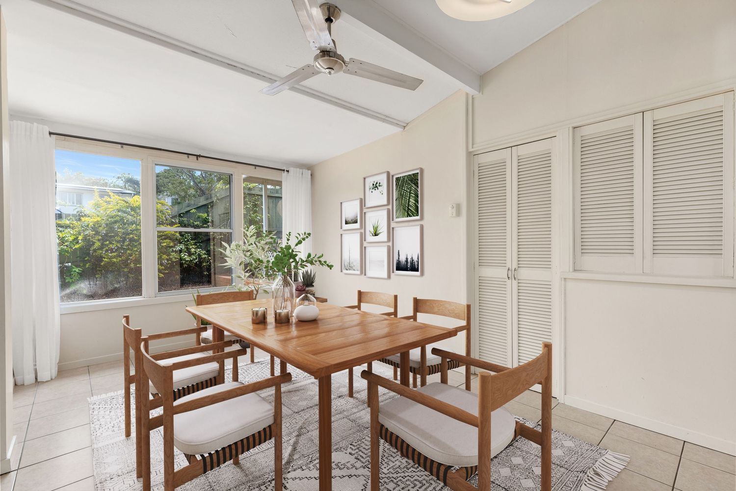 Airy dining room with timber table, louvred cupboards, and large garden-view windows.